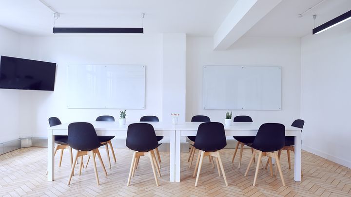 Heller Besprechungsraum mit langem Tisch, Stühlen und zwei leeren Whiteboards an der Wand
