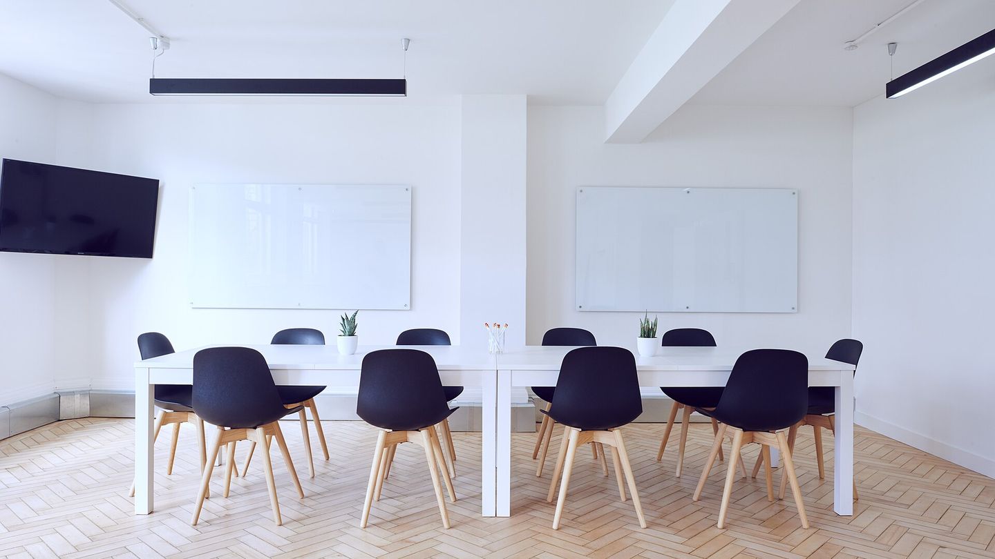 Heller Besprechungsraum mit langem Tisch, Stühlen und zwei leeren Whiteboards an der Wand