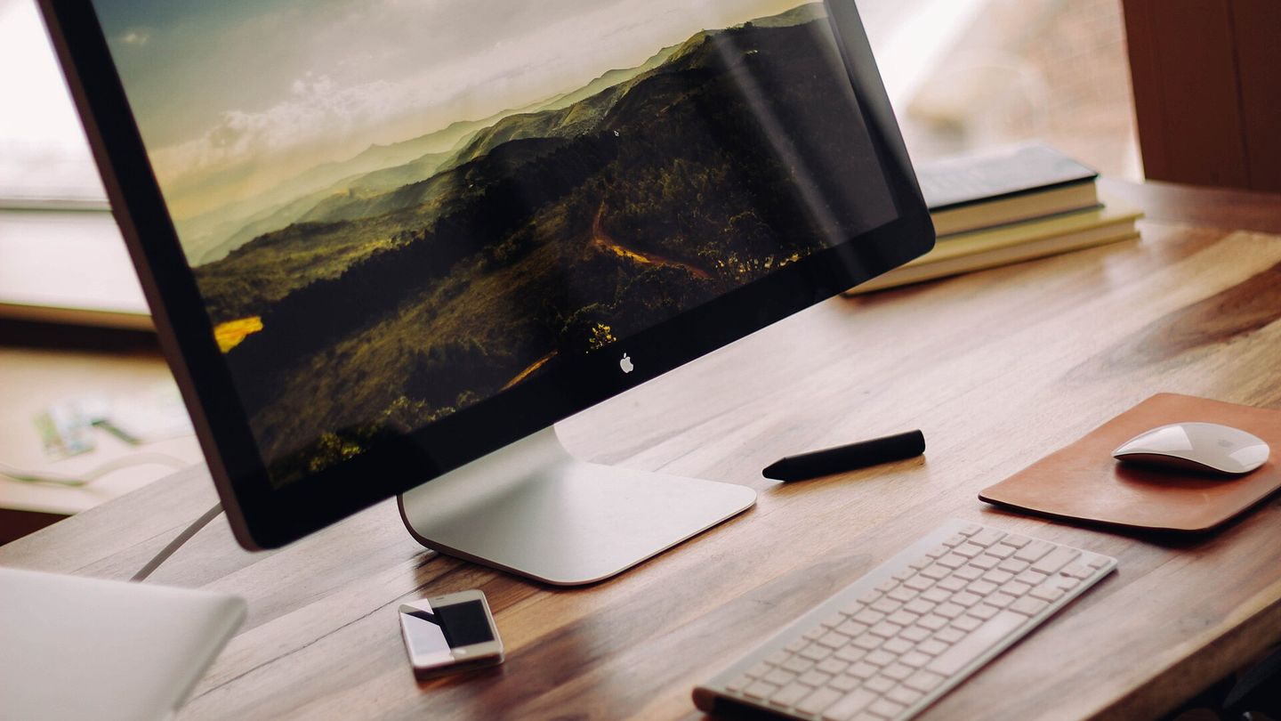 Aufgeräumter Schreibtisch aus Holz mit Monitor, Tastatur, Maus und Smartphone